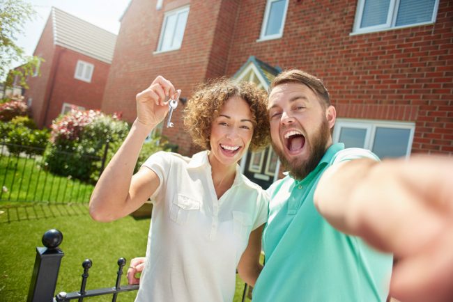 a young couple celebrate getting the keys to their new home by taking a selfie in the garden .