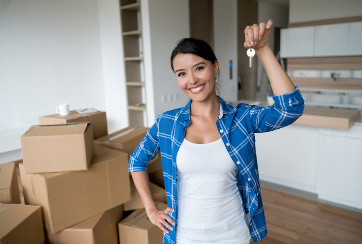 Happy young woman holding keys to her new house while packing and looking at the camera smiling - moving house concepts